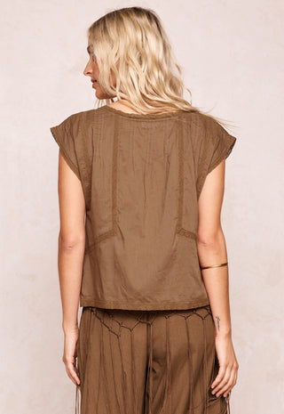 A woman shown from the back wearing a brown short-sleeve top and matching brown pants against a light beige textured background.